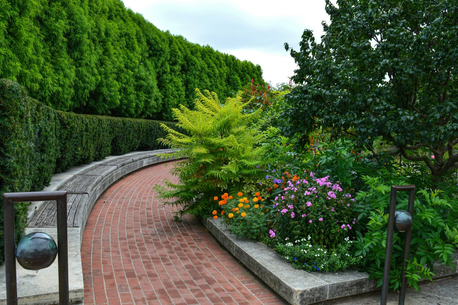 Geschwungener Klinkerweg zwischen Sitzmauer, Hecke und Staudenbeet